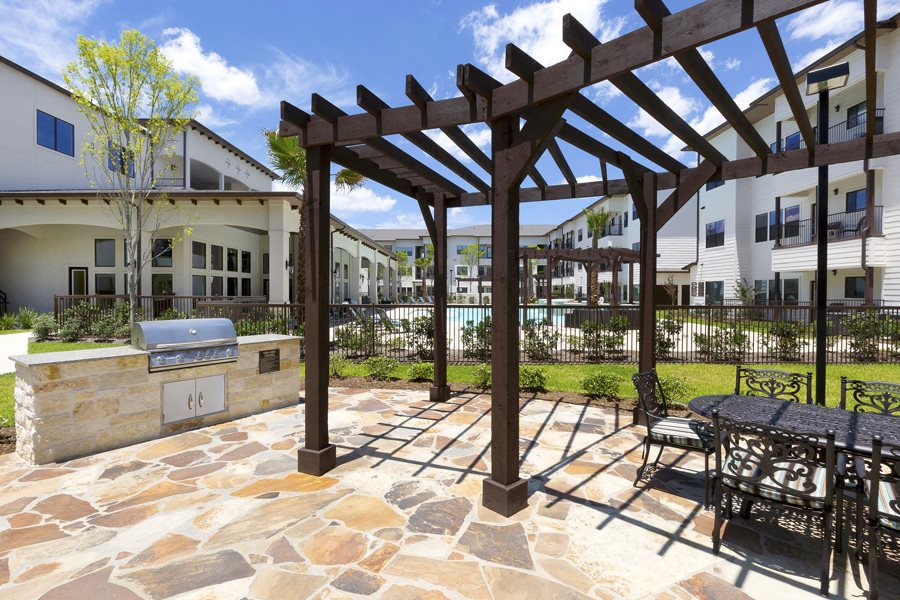 a patio with a grilling station and sitting area under a wooden pergola at a senior apartment community